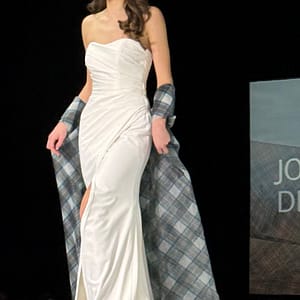 model in ivory wedding dress walking on catwalk with tartan organza cape flowing behind